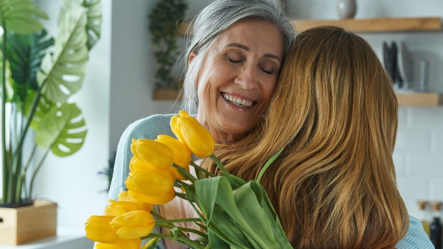 Egy anya és lánya megölelik egymást, az anya kezében sárga tulipán van 